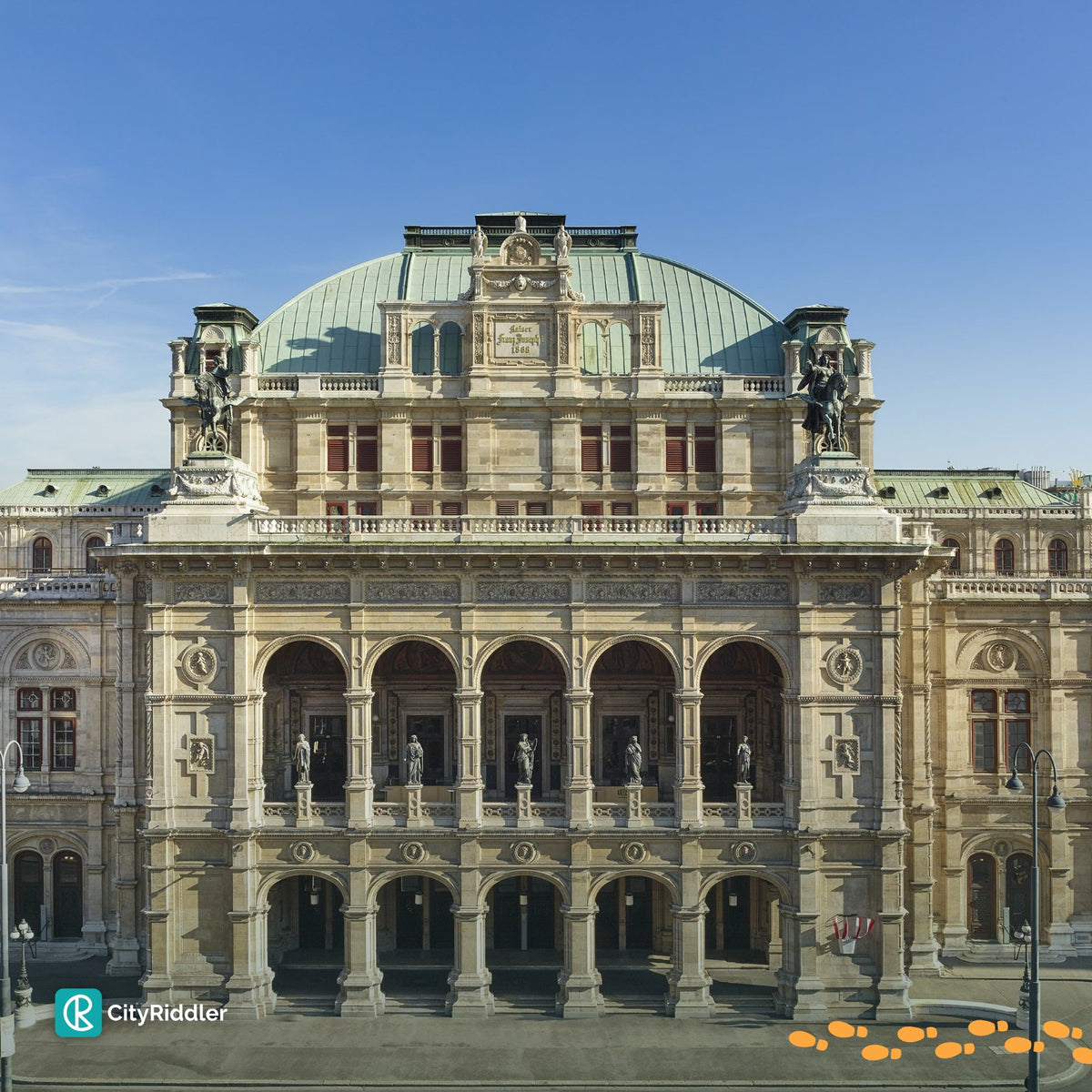 The grand facade of the Vienna State Opera under a clear blue sky, featuring a green dome, ornate stone columns, statues, and arched windows. A CityRiddler watermark is visible in the bottom-left corner.